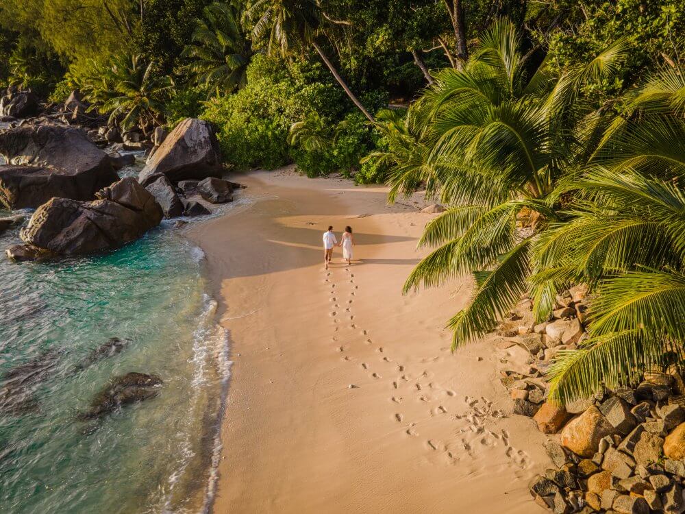 Foto de um casal caminhando pela areia na praia em Seychelles